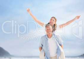 Middle aged couple piggy back against blurry sky and beach