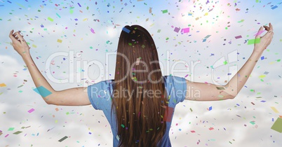 Back of woman with arms outstretched against sunny sky and confetti