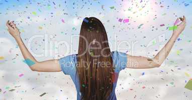 Back of woman with arms outstretched against sunny sky and confetti