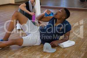 Tired male dancer with friend drinking water in studio