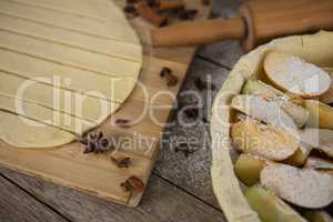 High angle view of pastry dough stripes on cutting board with apple in baking pan