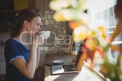 Woman with laptop drinking coffee in cafe
