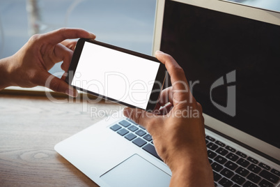 Cropped hand of man holding phone over laptop