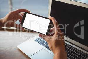 Cropped hand of man holding phone over laptop