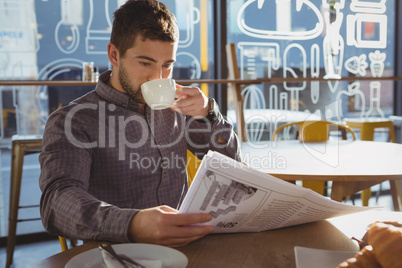 Businessman reading newspaper while drinking coffee in cafe