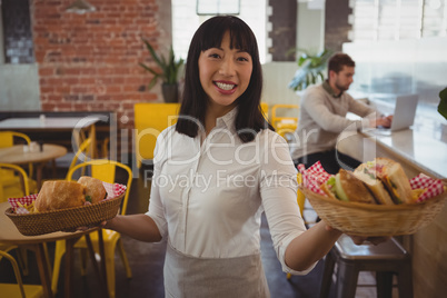 Portrait of waitress holding baskets with sandwiches while businessman using laptop