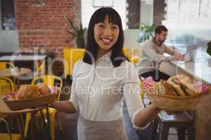 Portrait of waitress holding baskets with sandwiches while businessman using laptop