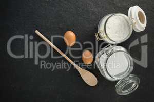 Overhead view of wooden spoon by eggs with sugar and flour in  jar