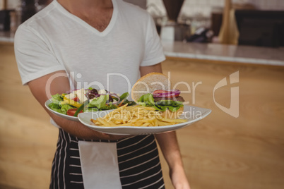 Mid section of waiter holding plate with food in cafe