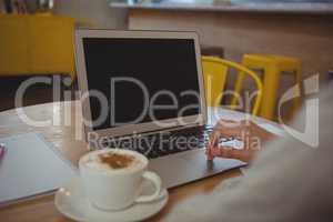 Cropped hand of businesswoman with coffee using laptop