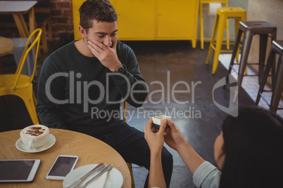 Woman gifting ring to boyfriend at cafe