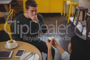 Woman gifting ring to boyfriend at cafe