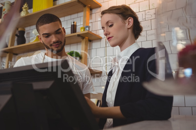 Female owner with waiter using cash register in cafe