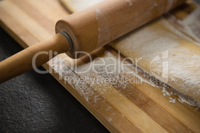 Cropped image of wooden rolling pin on dough over cutting board