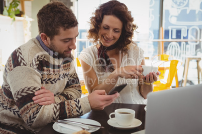 Man with woman using phone in cafe