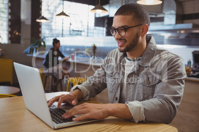 Man using laptop with friend in background at cafe