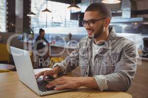 Man using laptop with friend in background at cafe