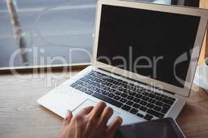 Cropped hand of man using laptop in cafe