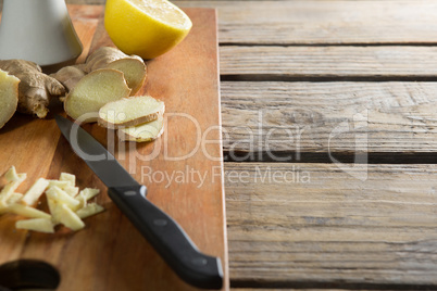 Close-up of ginger with lemon and knife on cutting board over table