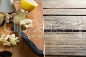 Close-up of ginger with lemon and knife on cutting board over table