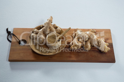 High angle view of ginger and powder in wooden plate on serving board