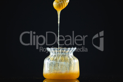 Honey dipper with flowing honey in glass jar