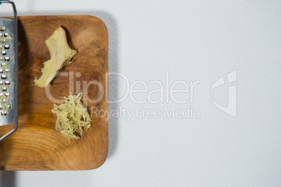 Directly above view of fresh ginger and steel grater on wooden plate