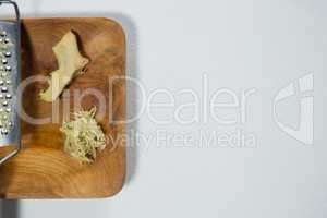 Directly above view of fresh ginger and steel grater on wooden plate