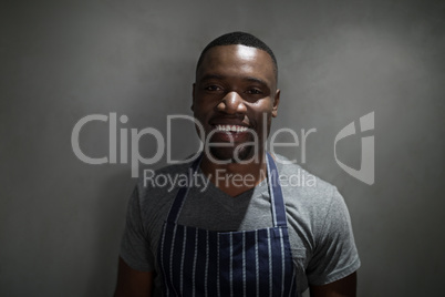 Portrait of happy waiter standing against grey background