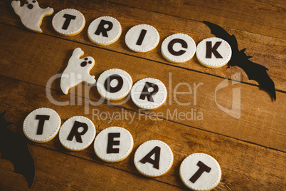 Cookies with trick or treat text by spooky decorations on wooden table