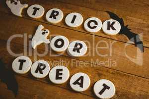 Cookies with trick or treat text by spooky decorations on wooden table