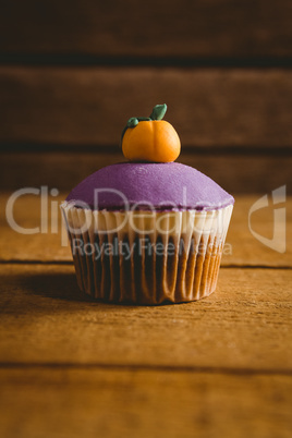 Purple cup cake with pumpkin icing on wooden table