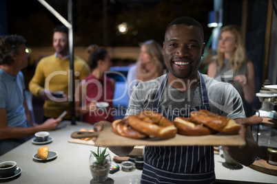 Portrait of happy waiter holding sweet food in wooden tray