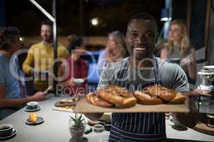 Portrait of happy waiter holding sweet food in wooden tray