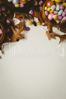 Overhead view of candies in wooden bowl with autumn leaves