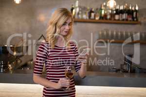 Beautiful woman using mobile phone while having wine