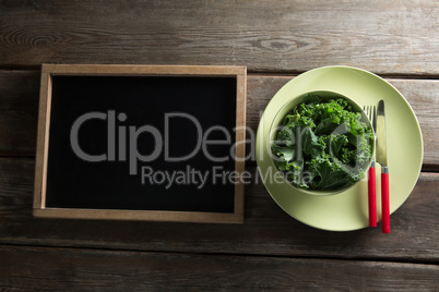 Overhead view of kale in bowl on plate by blackboard
