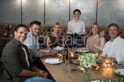 Portrait of happy waitress and customers at dining table
