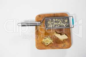 High angle view of steel grater and fresh ginger on wooden plate