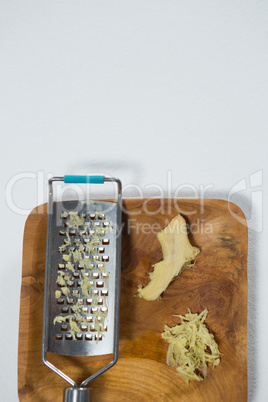 Overhead view of fresh ginger and steel grater on wooden plate