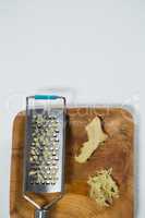Overhead view of fresh ginger and steel grater on wooden plate