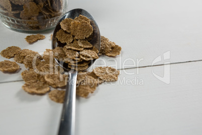 Wheat flakes in spoon on table