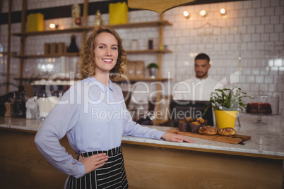 Portrait of smiling waitress standing with hand on hip by counter