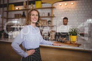 Portrait of smiling waitress standing with hand on hip by counter