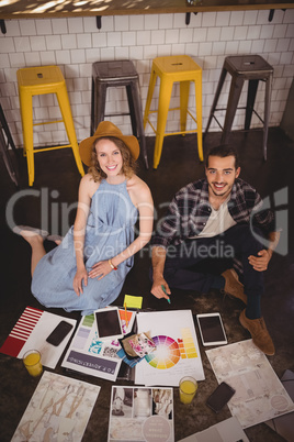 High angle portrait of smiling young creative professionals sitting on floor with sheets