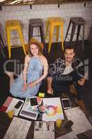 High angle portrait of smiling young creative professionals sitting on floor with sheets