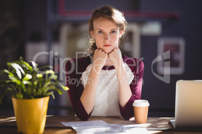 Portrait of confident young designer sitting with disposable coffee cup and sheets