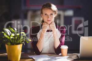 Portrait of confident young designer sitting with disposable coffee cup and sheets