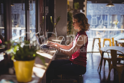 Side view of young woman using laptop at coffee shop