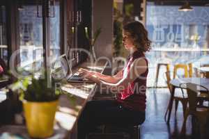 Side view of young woman using laptop at coffee shop